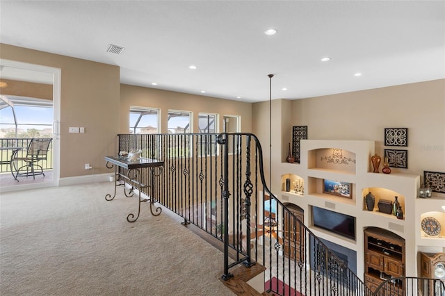 hallway with an upstairs landing, carpet flooring, built in features, baseboards, and visible vents