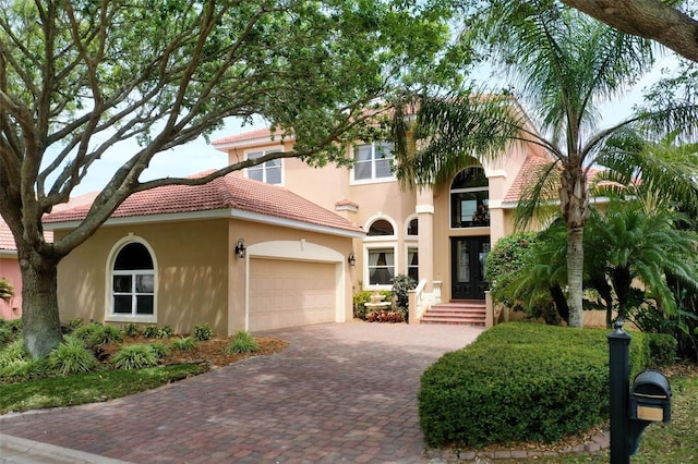 mediterranean / spanish home featuring decorative driveway, stucco siding, a tiled roof, and a garage