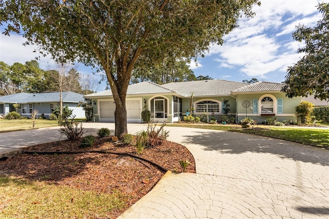 ranch-style home featuring a front yard, stucco siding, a garage, a tiled roof, and decorative driveway