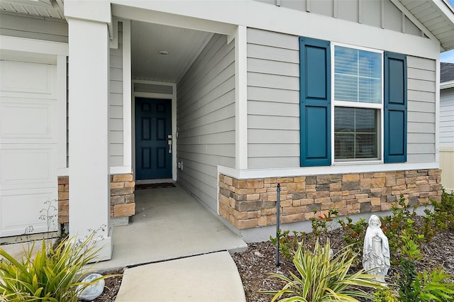 doorway to property with a garage, stone siding, and board and batten siding