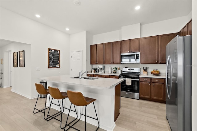 kitchen with a breakfast bar area, a sink, light countertops, appliances with stainless steel finishes, and a center island with sink