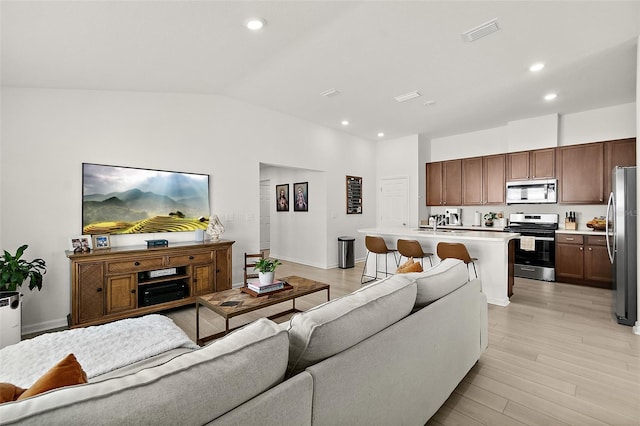 living area with vaulted ceiling, light wood finished floors, visible vents, and recessed lighting