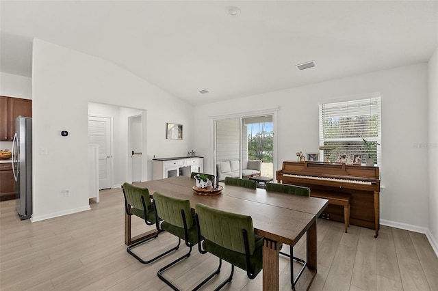 dining room featuring light wood-style floors, visible vents, vaulted ceiling, and baseboards