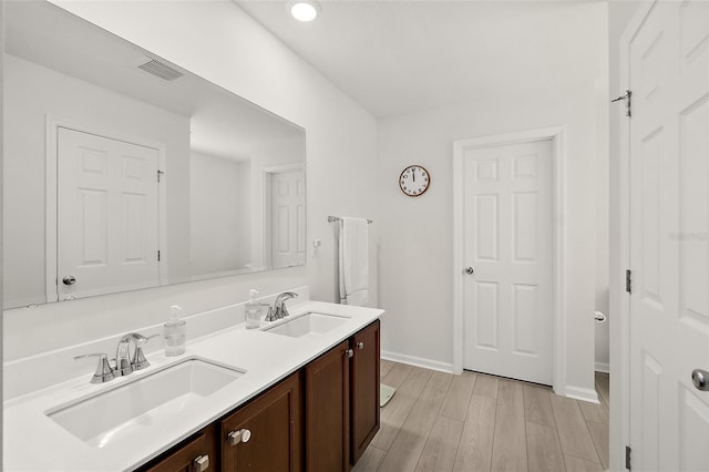 bathroom with double vanity, visible vents, a sink, and wood finished floors