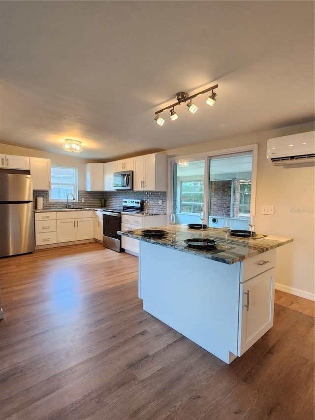 kitchen featuring stainless steel appliances, an AC wall unit, white cabinetry, and a sink