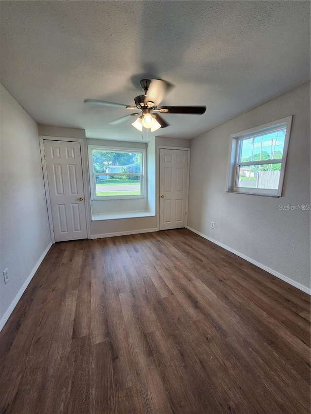 unfurnished bedroom with a textured ceiling, multiple windows, baseboards, and dark wood-type flooring