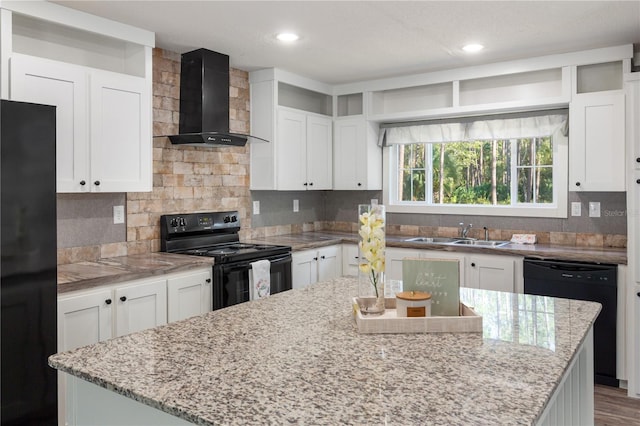 kitchen with white cabinets, wall chimney exhaust hood, a kitchen island, black appliances, and a sink