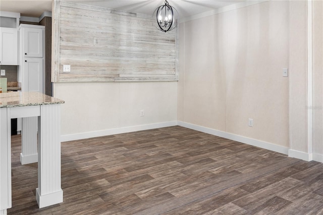 unfurnished dining area featuring dark wood-style floors, baseboards, and a notable chandelier