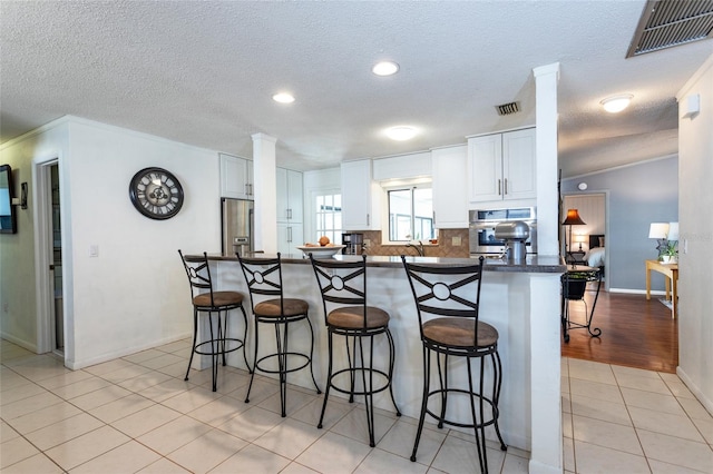 kitchen with visible vents, dark countertops, stainless steel appliances, a breakfast bar area, and light tile patterned floors