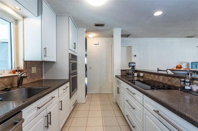 kitchen with dark countertops, light tile patterned floors, appliances with stainless steel finishes, white cabinetry, and a sink