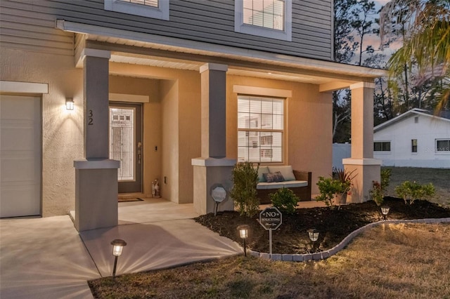 exterior entry at dusk featuring an attached garage and stucco siding