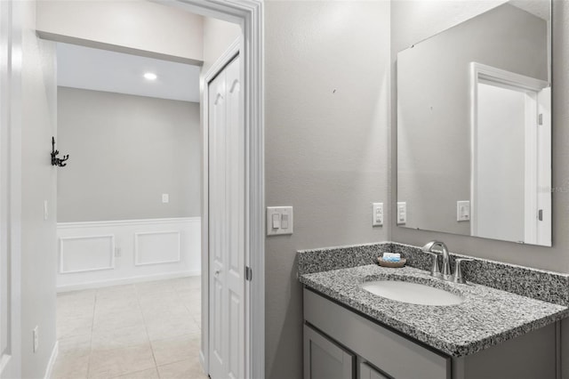 bathroom with a wainscoted wall, tile patterned flooring, vanity, and a decorative wall