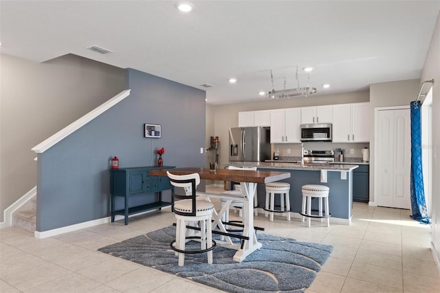 kitchen featuring visible vents, a kitchen island with sink, stainless steel appliances, light tile patterned flooring, and white cabinets