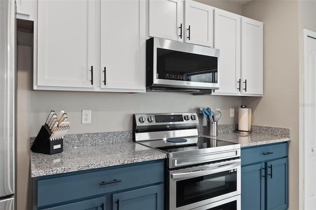 kitchen with blue cabinetry, light stone counters, white cabinets, and appliances with stainless steel finishes