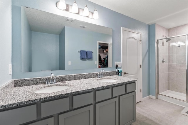 bathroom with double vanity, a spacious closet, a stall shower, and a sink