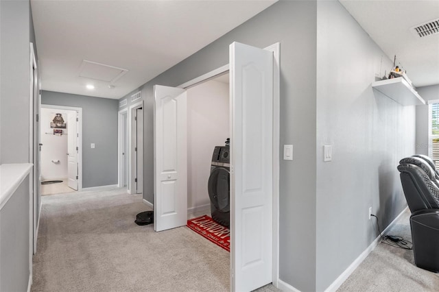 hallway featuring visible vents, baseboards, attic access, light carpet, and washer / dryer