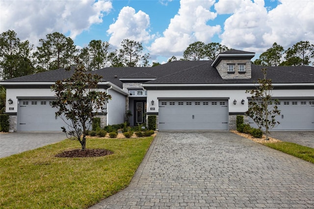 view of front of home featuring decorative driveway, stucco siding, a garage, stone siding, and a front lawn