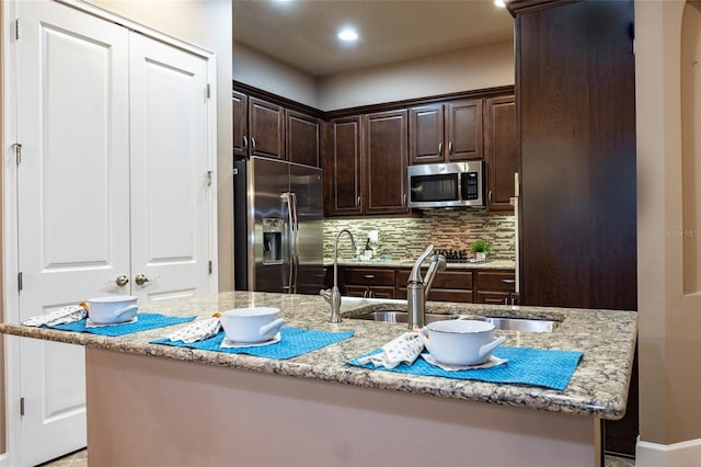 kitchen with decorative backsplash, appliances with stainless steel finishes, light stone countertops, dark brown cabinets, and a sink