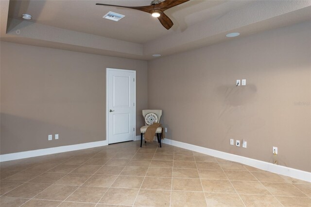 unfurnished room with a ceiling fan, a tray ceiling, baseboards, and light tile patterned floors