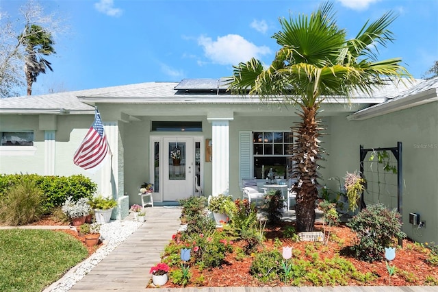 doorway to property featuring covered porch, roof mounted solar panels, and stucco siding