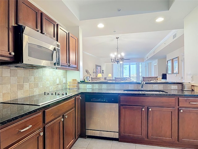 kitchen with dark stone counters, an inviting chandelier, a sink, stainless steel appliances, and backsplash