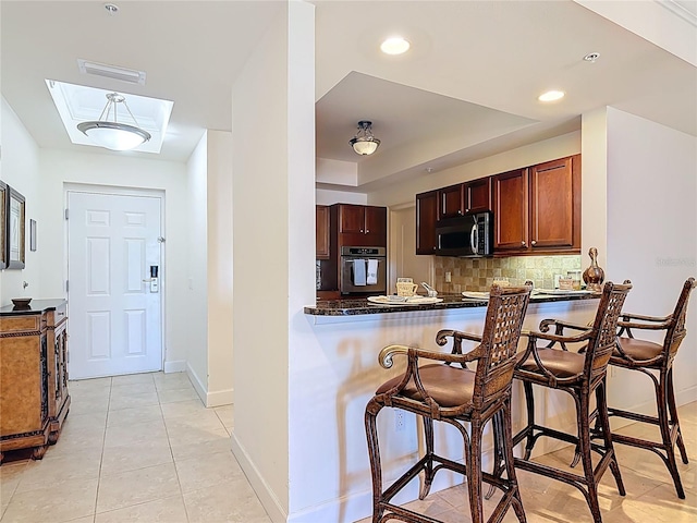 kitchen featuring a breakfast bar area, dark countertops, stainless steel appliances, a raised ceiling, and tasteful backsplash