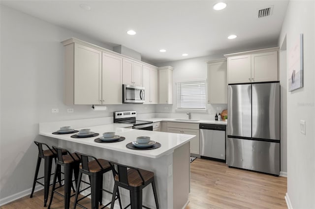 kitchen featuring a peninsula, a sink, stainless steel appliances, light countertops, and a kitchen breakfast bar