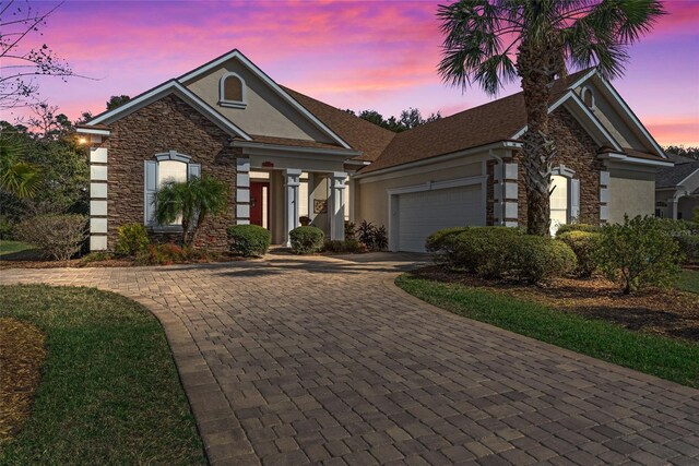 view of front facade featuring stucco siding, stone siding, a garage, and decorative driveway