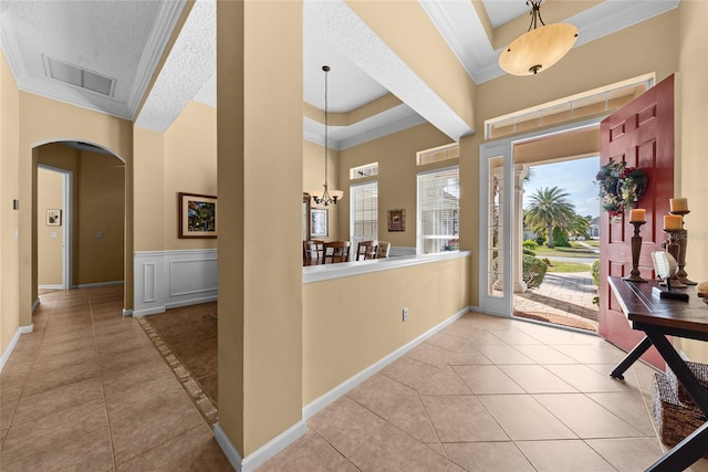 entrance foyer featuring visible vents, tile patterned floors, ornamental molding, arched walkways, and a raised ceiling