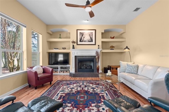 living area featuring built in features, wood finished floors, visible vents, and a textured ceiling