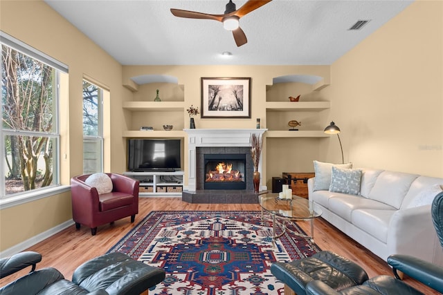 living area featuring built in features, wood finished floors, visible vents, and a textured ceiling