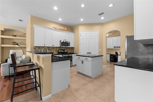 kitchen featuring a center island, a peninsula, arched walkways, white cabinets, and stainless steel appliances