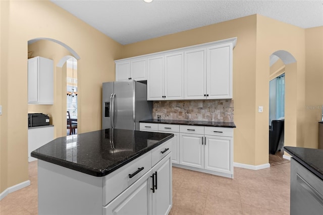 kitchen with backsplash, dark stone countertops, arched walkways, stainless steel fridge, and white cabinetry