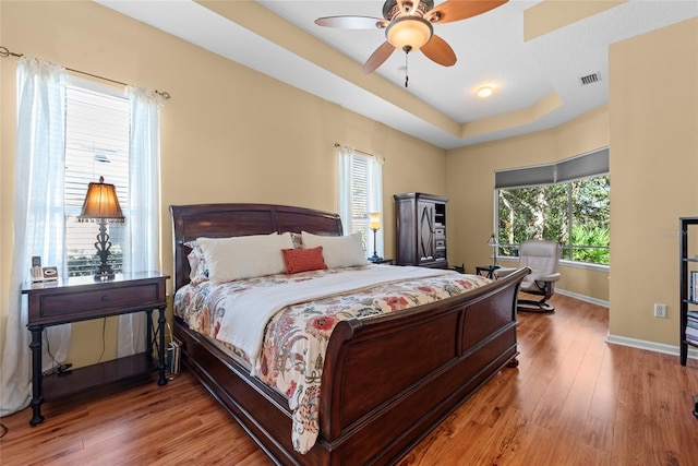 bedroom featuring visible vents, wood finished floors, baseboards, a raised ceiling, and ceiling fan