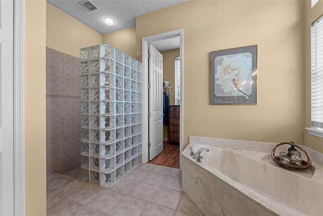 full bath featuring a textured ceiling, visible vents, walk in shower, a garden tub, and tile patterned floors