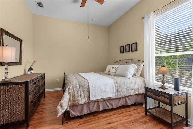 bedroom with visible vents, light wood-style flooring, a textured ceiling, baseboards, and ceiling fan