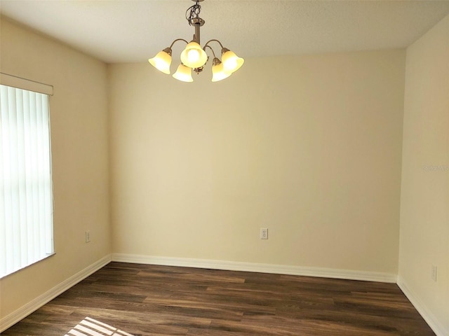 spare room featuring a notable chandelier, dark wood-type flooring, and baseboards