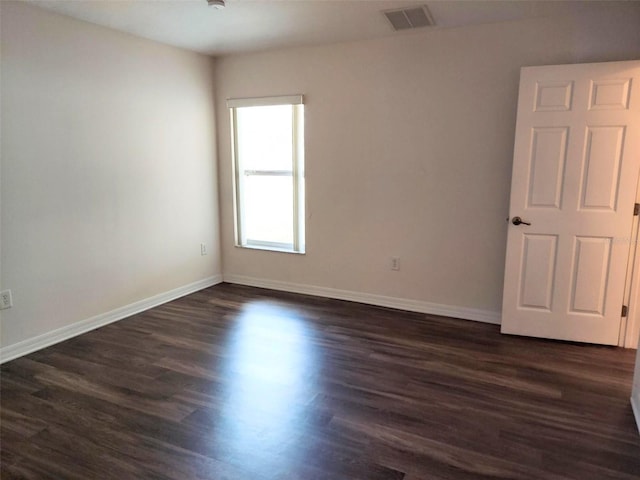 empty room featuring visible vents, baseboards, and dark wood-style flooring