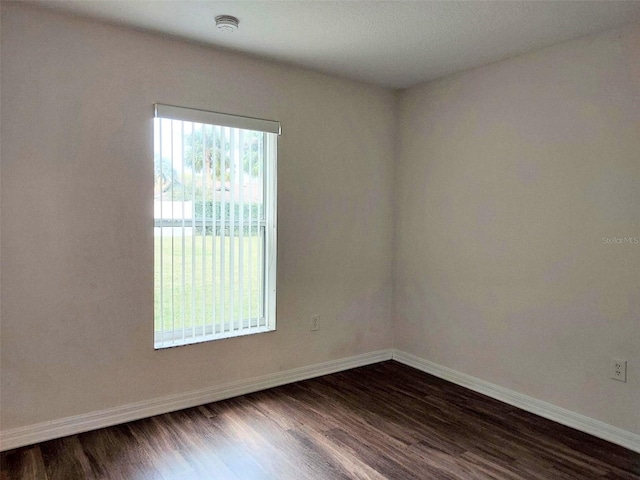 spare room featuring dark wood-type flooring and baseboards