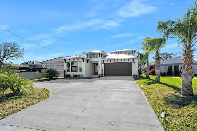 prairie-style home with stucco siding, driveway, metal roof, a front yard, and a garage