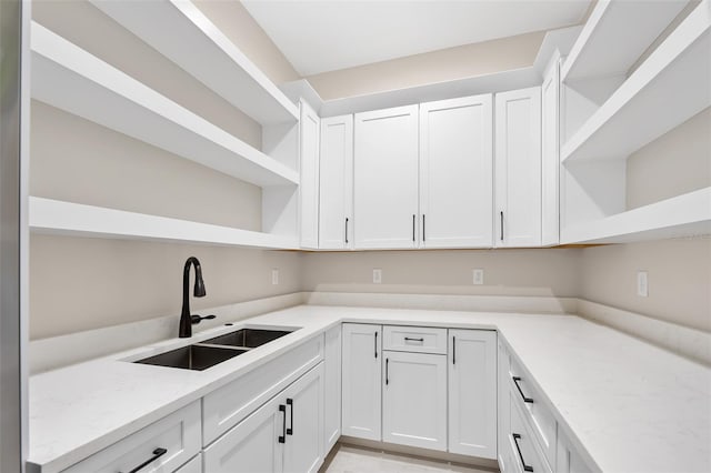 kitchen featuring light stone counters, a sink, white cabinetry, and open shelves