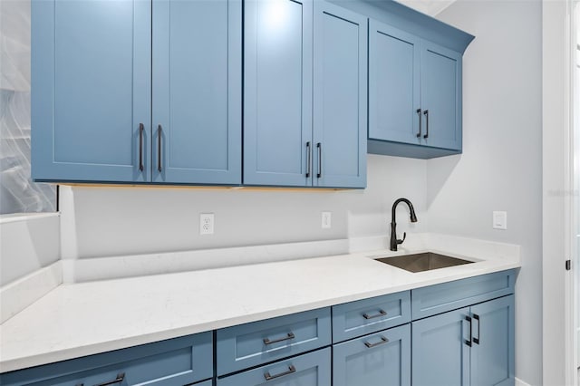 kitchen featuring blue cabinetry, light stone counters, and a sink