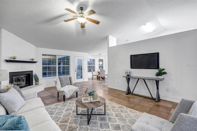 tiled living room with ceiling fan, vaulted ceiling, a fireplace, and a textured ceiling