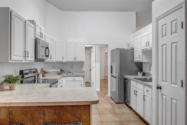 kitchen with light countertops, a peninsula, appliances with stainless steel finishes, and a sink