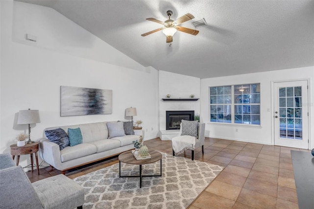 living room with visible vents, a large fireplace, vaulted ceiling, a textured ceiling, and a ceiling fan