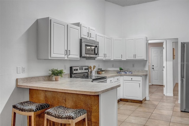 kitchen featuring a breakfast bar area, light tile patterned floors, a peninsula, stainless steel appliances, and light countertops