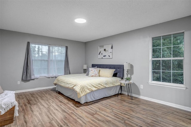 bedroom with baseboards, a textured ceiling, and wood finished floors
