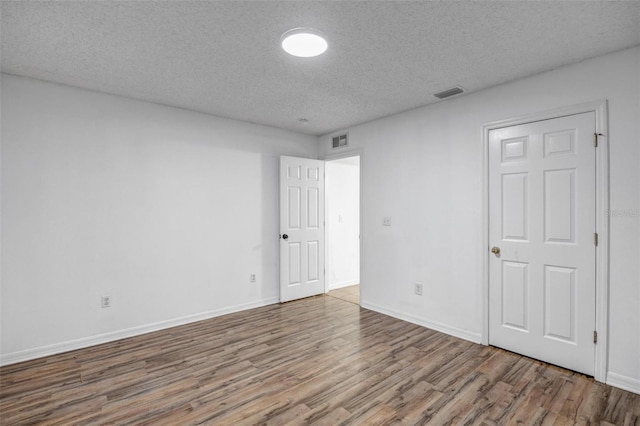 spare room with visible vents, a textured ceiling, baseboards, and wood finished floors