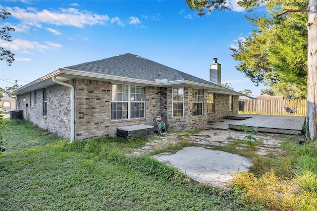 rear view of property with cooling unit, roof with shingles, a chimney, a deck, and a lawn