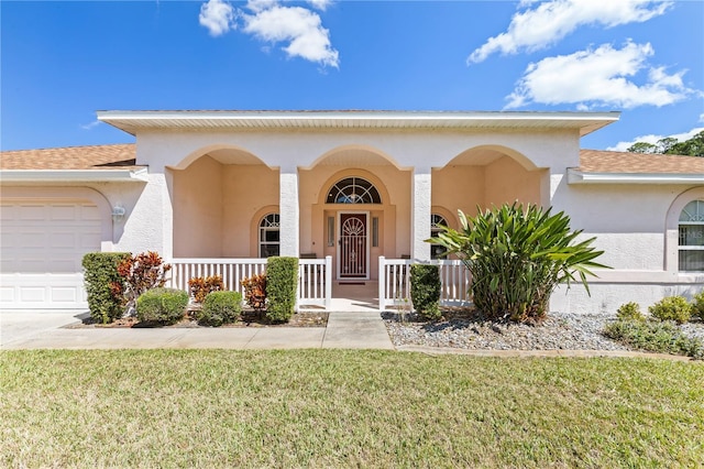 view of front of property with covered porch, a front lawn, a garage, and stucco siding